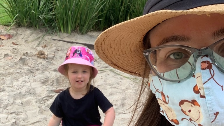 Woman wearing a mask takes a selfie with a child in a sandpit.