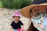 Woman wearing a mask takes a selfie with a child in a sandpit.