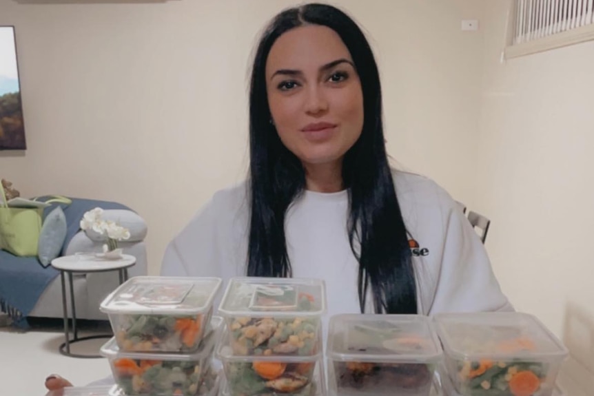 A photo of Elvan with many plastic containers of food stacked up in front of her.