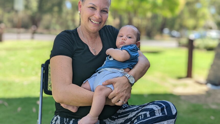 Woman holding baby while sitting in garden setting.