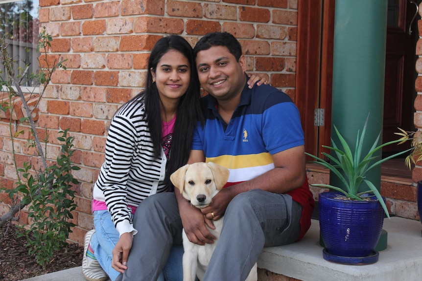 A woman and a man on their doorstep, with a labrador puppy.