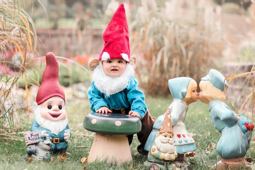 Baby dressed as garden gnome surrounded by garden gnomes