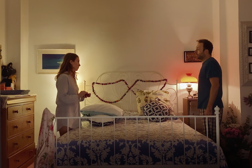 A couple stand on either side of a bed in the web series Cancelled