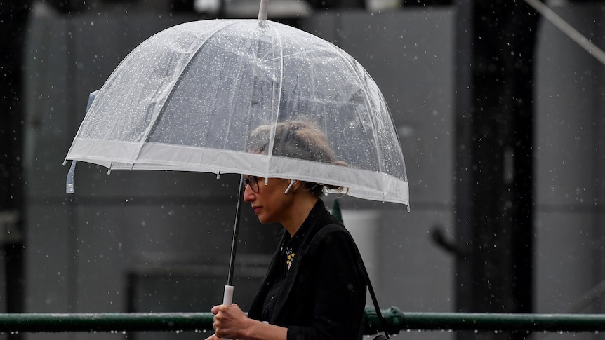 a woman walks down a street holding a clear umbrella over her head, rain drops can be seen in the background