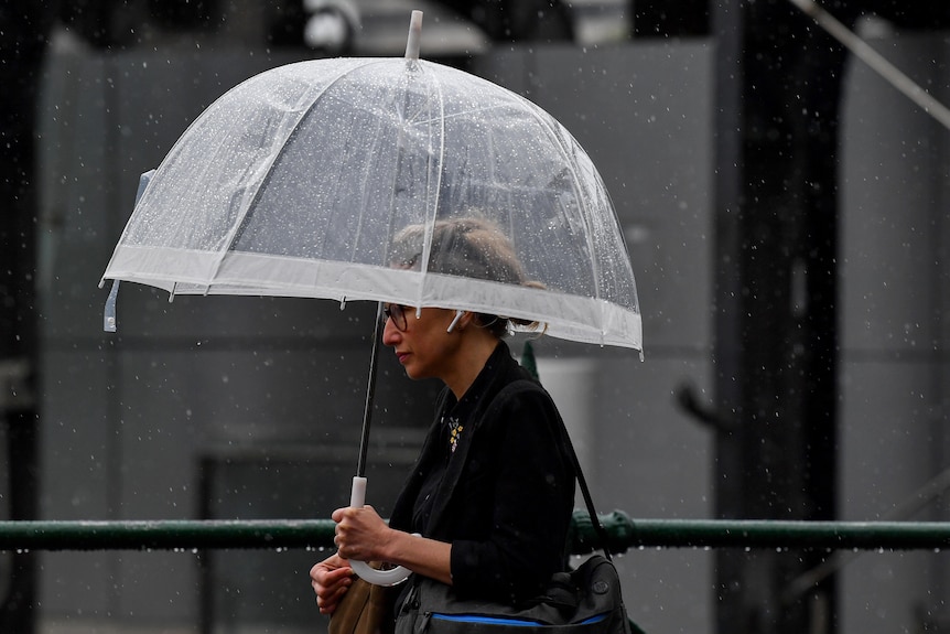 a woman walks down a street holding a clear umbrella over her head, rain drops can be seen in the background