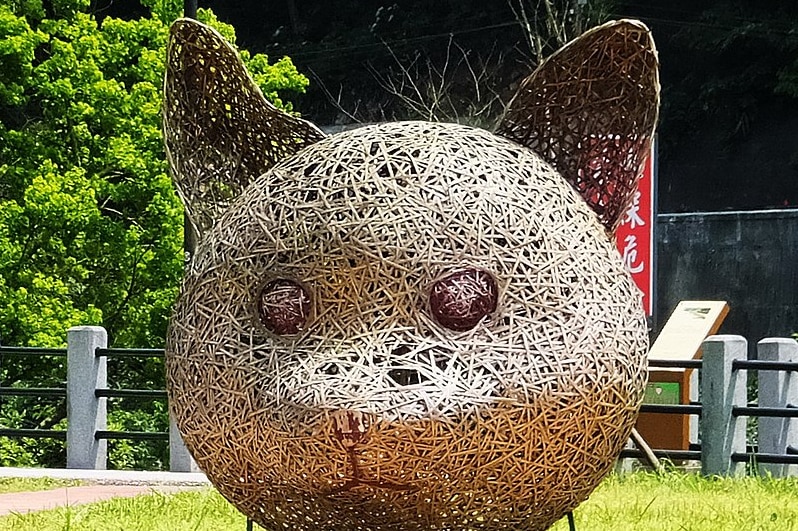 A giant twine cat head watches over a street path.