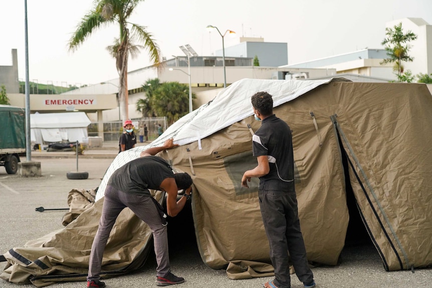 Two men setting up a tent in a car park