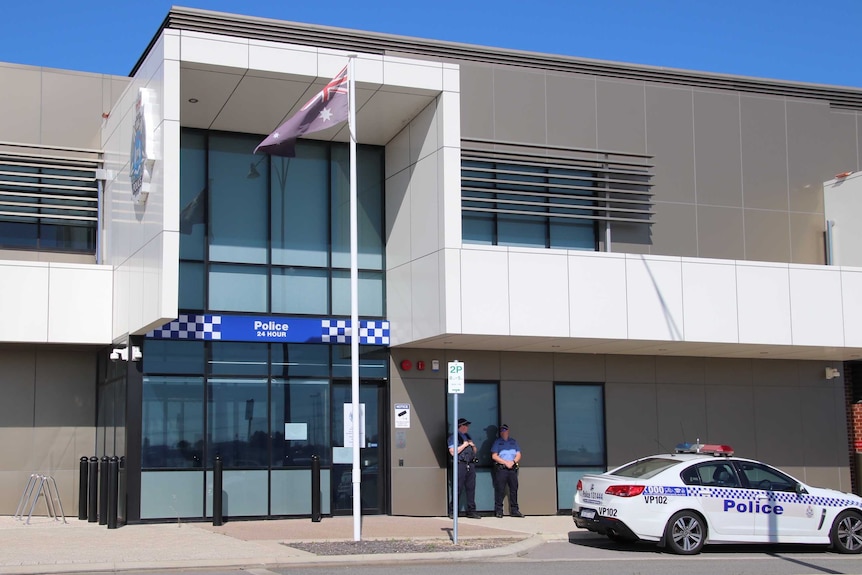 Exterior shot of Cockburn police station with two police officers standing outside, flag flying and a police car parked outside.