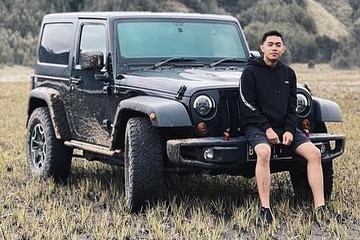 A young man sits on the hood of a black Jeep