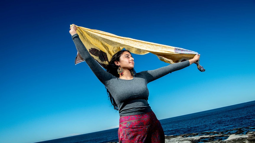 On a bright day, you see a woman of Indian descent waving her scarf near Clovelly beach.