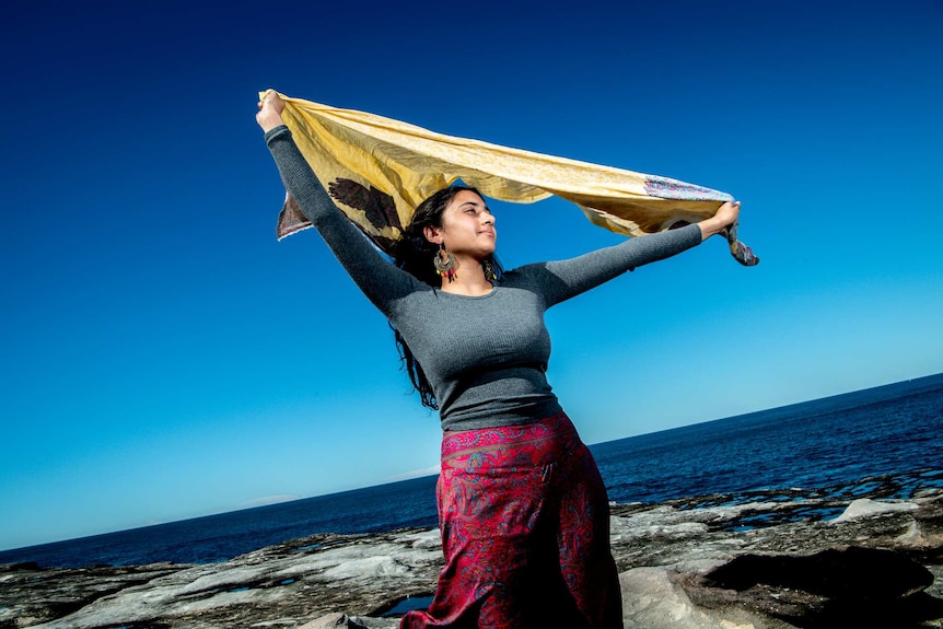 On a bright day, you see a woman of Indian descent waving her scarf near Clovelly beach.