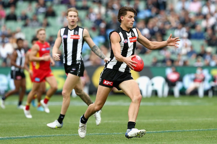 A Collingwood AFL player runs inside the 50m arc and looks up as he gets ready to kick the ball.