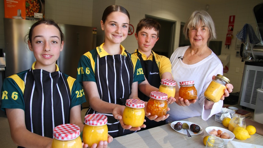 Three students stand with a teacher, Sue White holding jars of lemon curd. 