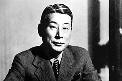 A black and white photo shows a Japanese man in a suit looking into the camera.
