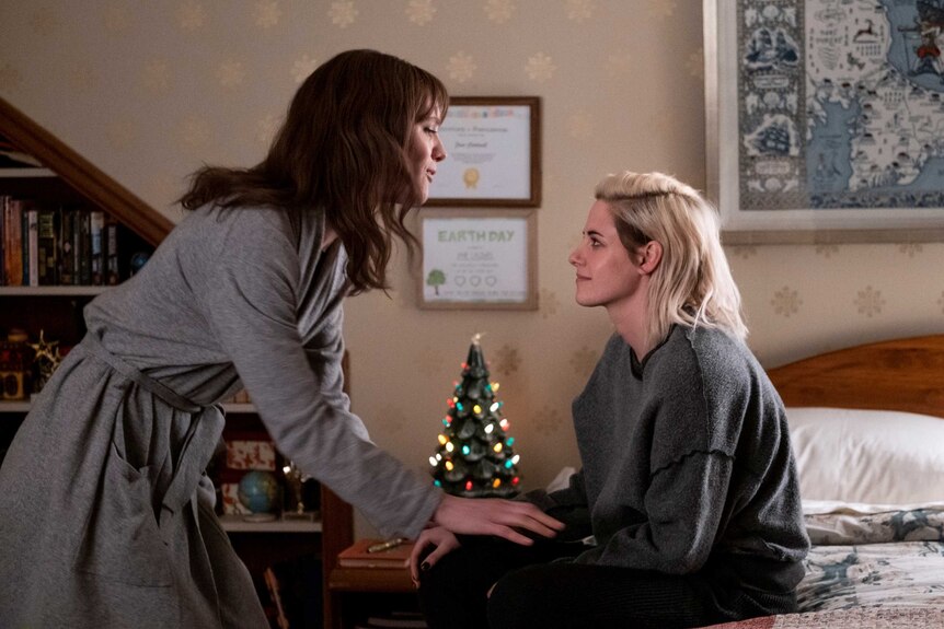 Actors Mackenzie Davis and Kristen Stewart talking in a bedroom in the movie Happiest Season