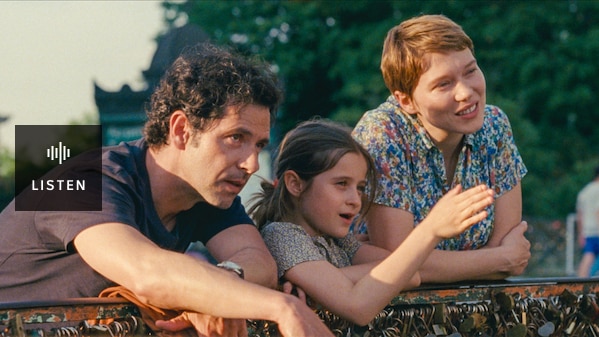 A couple and their young daughter lean over a fence, looking at something out of shot. The sunlight shines on their faces. Has Audio