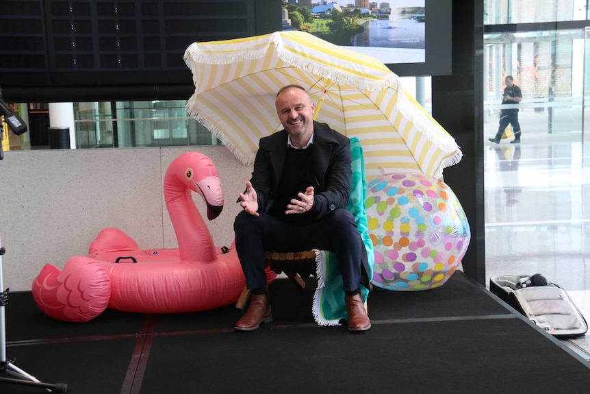 Chief Minister Andrew Barr sits on a made up beach scene at Canberra Airport.
