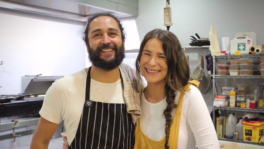 Two chefs embrace while posing for a photo inside a commercial kitchen