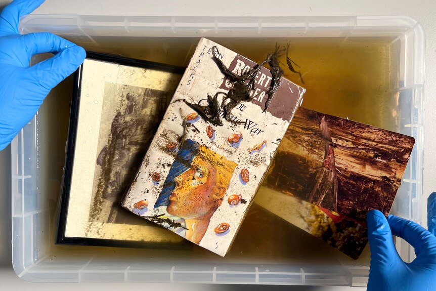 Two photos and a book being rinsed in a plastic container of water.