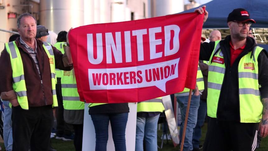 A photo of milk workers outside a factory holding a United Workers Union sign