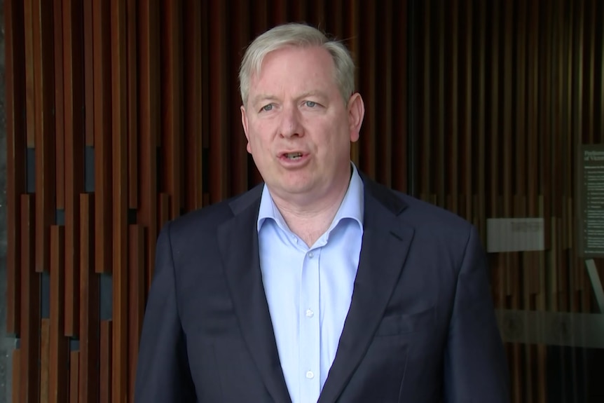 A man in a suit and blue shirt talks to the camera.