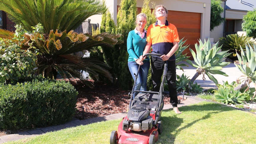 Zoe Sandell (l) and Brodie Lunn standing on the lawn in front of a house with Brodie's lawnmower