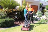 Zoe Sandell (l) and Brodie Lunn standing on the lawn in front of a house with Brodie's lawnmower