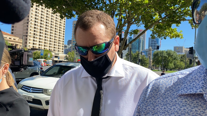 A man wearing a black face mask in front of tall buildings