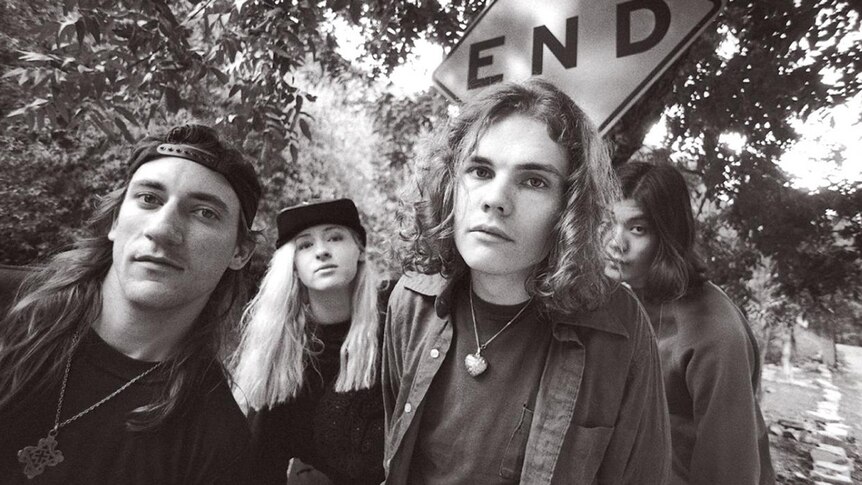Black and white photo of four members of Smashing Pumpkins standing in front of a street sign that says END
