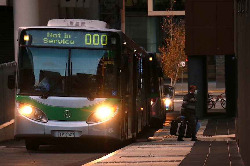 A man in a face mask walks away from a Transperth bus at dusk towards a hotel.