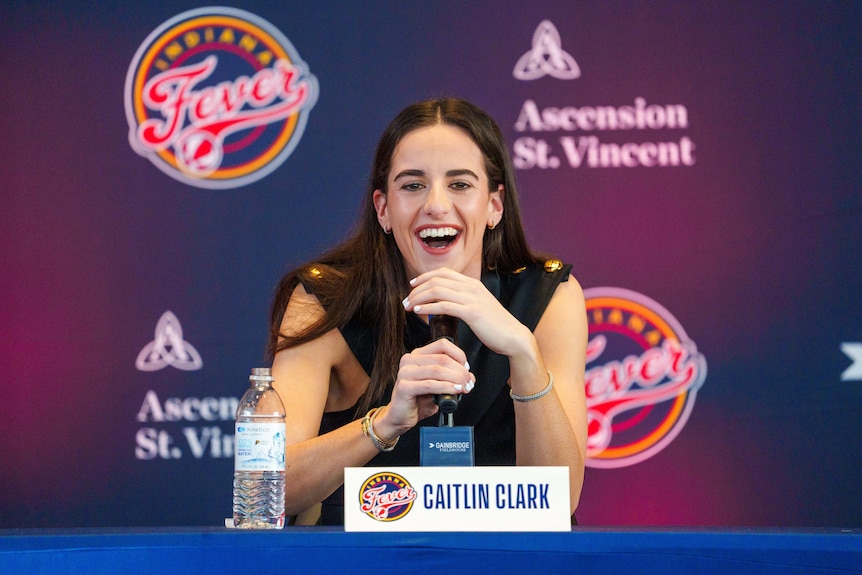 Caitlin Clark sits at a microphone at a press conference 