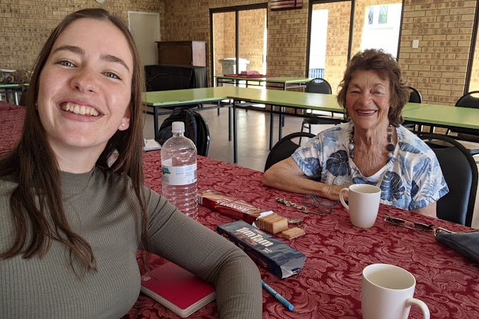 A young girl takes a selfie with an older woman across the table they are sharing biccies and tea