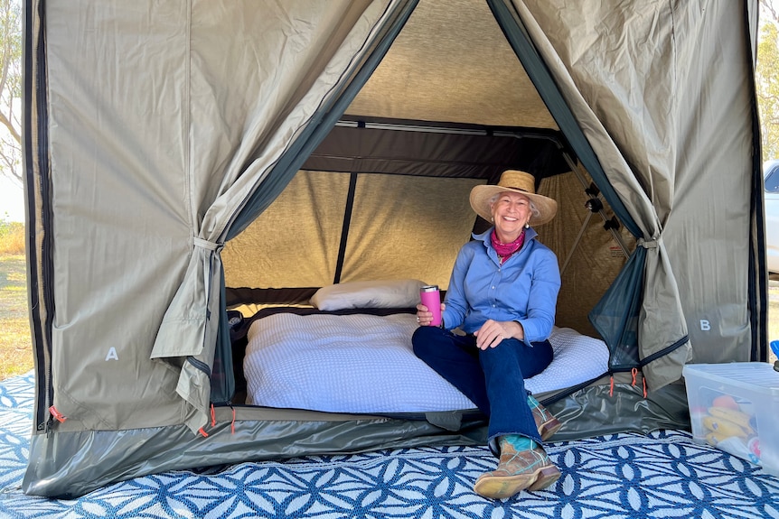A woman wearing a cowboy hat sits in her tent smiling out.