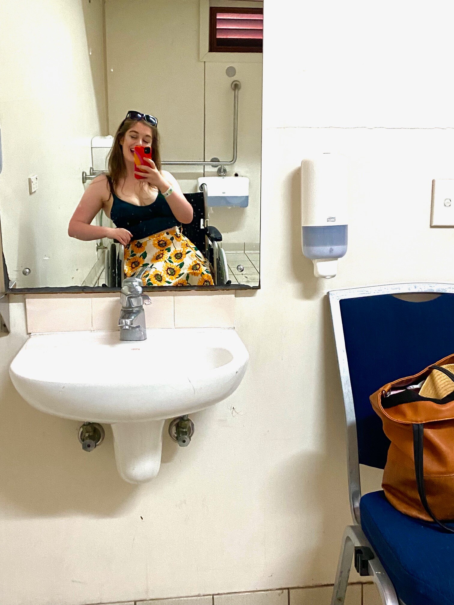 A young woman in a wheelchair takes a selfie in a bathroom mirror