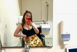 A young woman in a wheelchair takes a selfie in a bathroom mirror