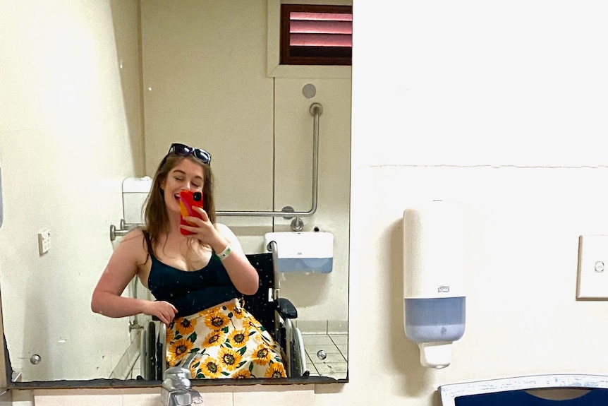 A young woman in a wheelchair takes a selfie in a bathroom mirror