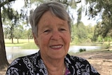 Older woman with grey hair smiling at the camera with a park and lake in the background.