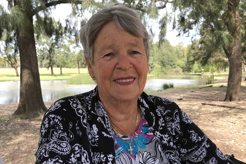 Older woman with grey hair smiling at the camera with a park and lake in the background.
