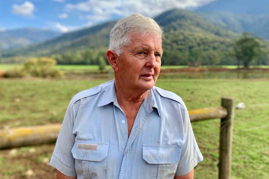 Farmer Bruce Lumsden stands on his farm in Bright. The paddock behind him is green, there are hills on the horizon.