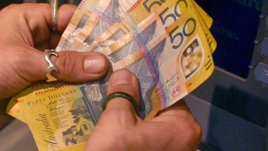 A customer counts his Australian fifty dollar notes after using an ATM machine