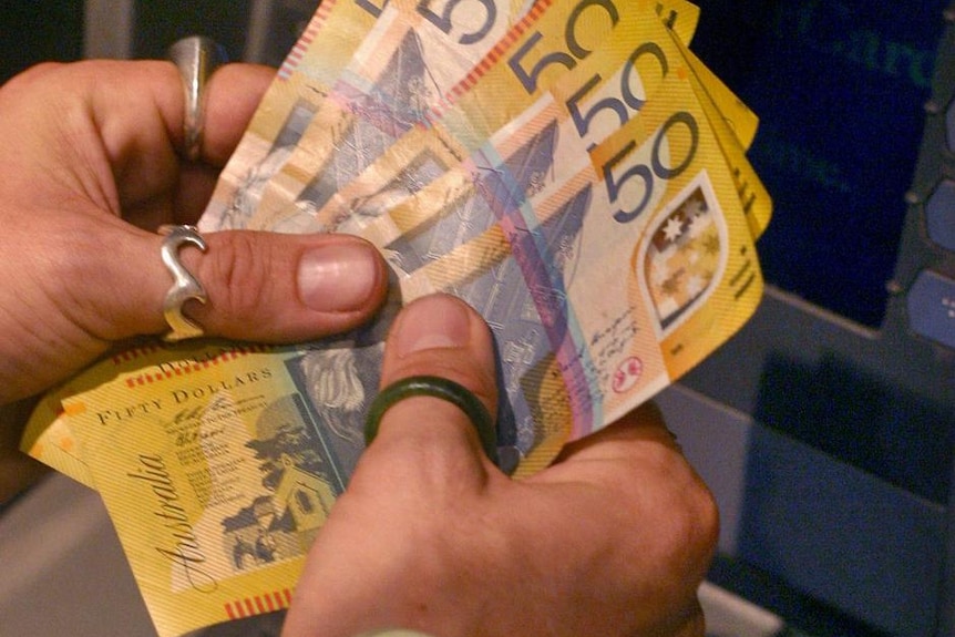 A customer counts his Australian fifty dollar notes after using an ATM machine