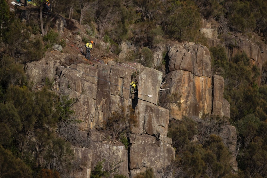 Two men abseil down a rock wall
