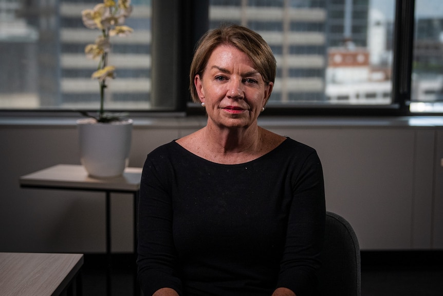 A woman with short hair sits in an office wearing a black top.