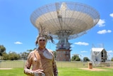 A man in traditional Wiradjuri dress stands in front of the Parkes radio telescope.