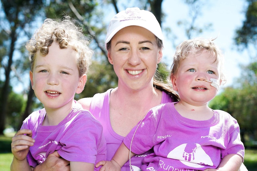 A woman holding two young boys, one with an oxygen tube in his nose, all wearing purple