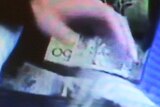 A still from CCTV footage shows a hand removing wads of $50 notes from a blue cooler bag.