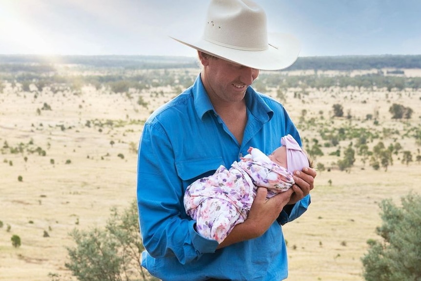 Graham holds his baby daughter with paddocks in the background.