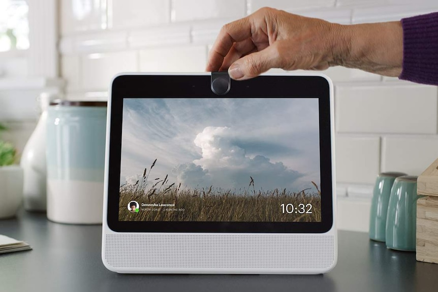 A person places a physical cover over the camera on the Facebook Portal smart speaker.
