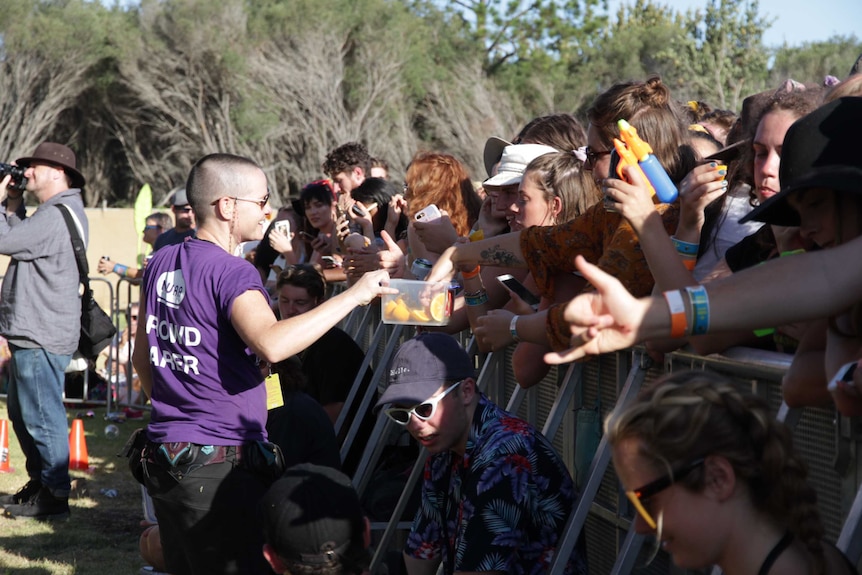 Girl walking along a music barrier handing out orange slices to crowds waiting for a band