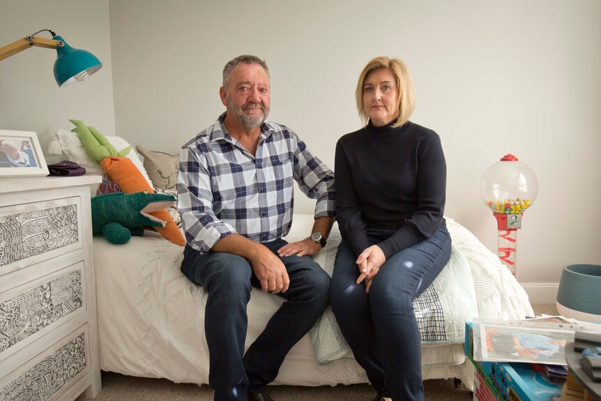 Two middle aged white people, a man and a woman, sitting on a bed in a kid's bedroom